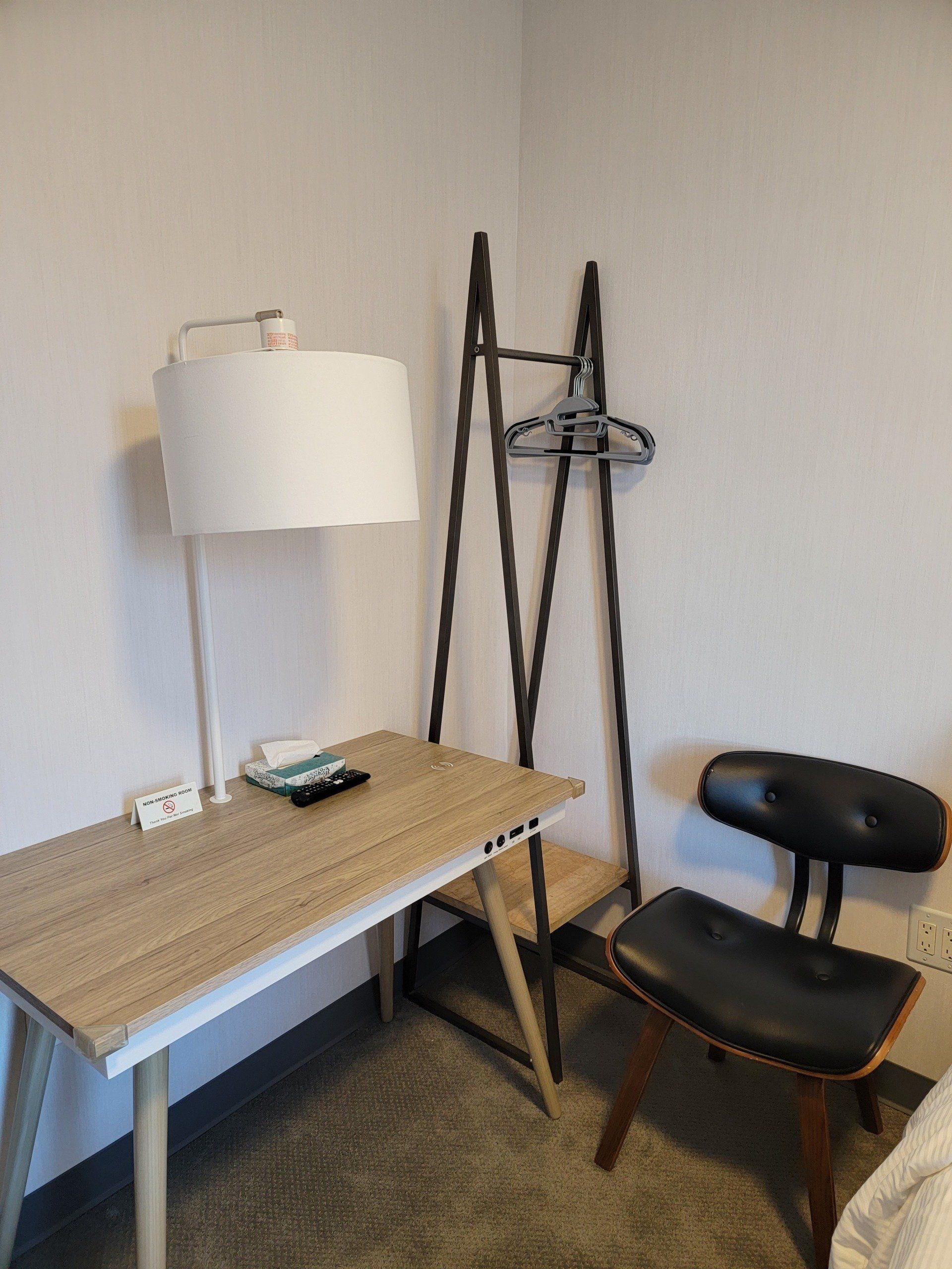 A bedroom with a desk , chair , lamp and clothes rack.