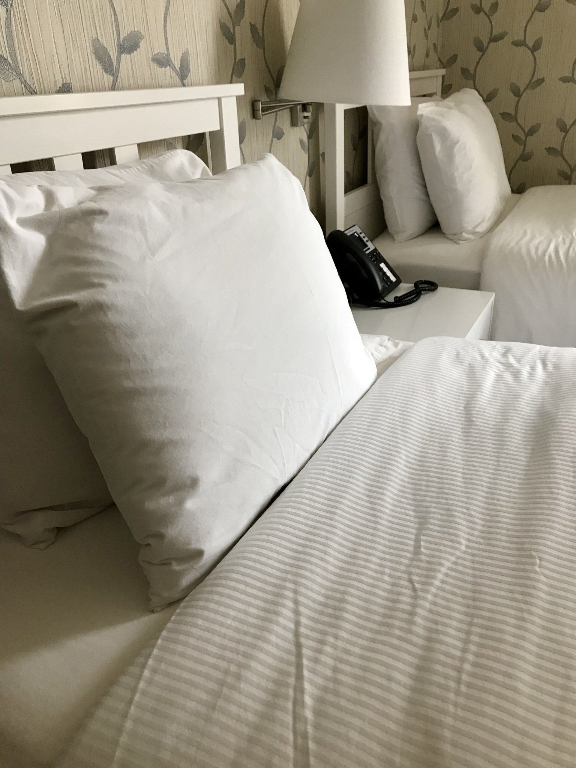 A bed with white sheets and pillows in a hotel room
