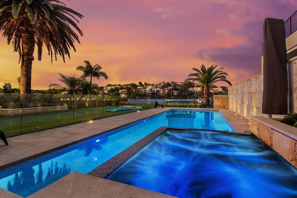 A large swimming pool with palm trees in the background at sunset — Dimension One Glass Fencing In Tuggerah, NSW