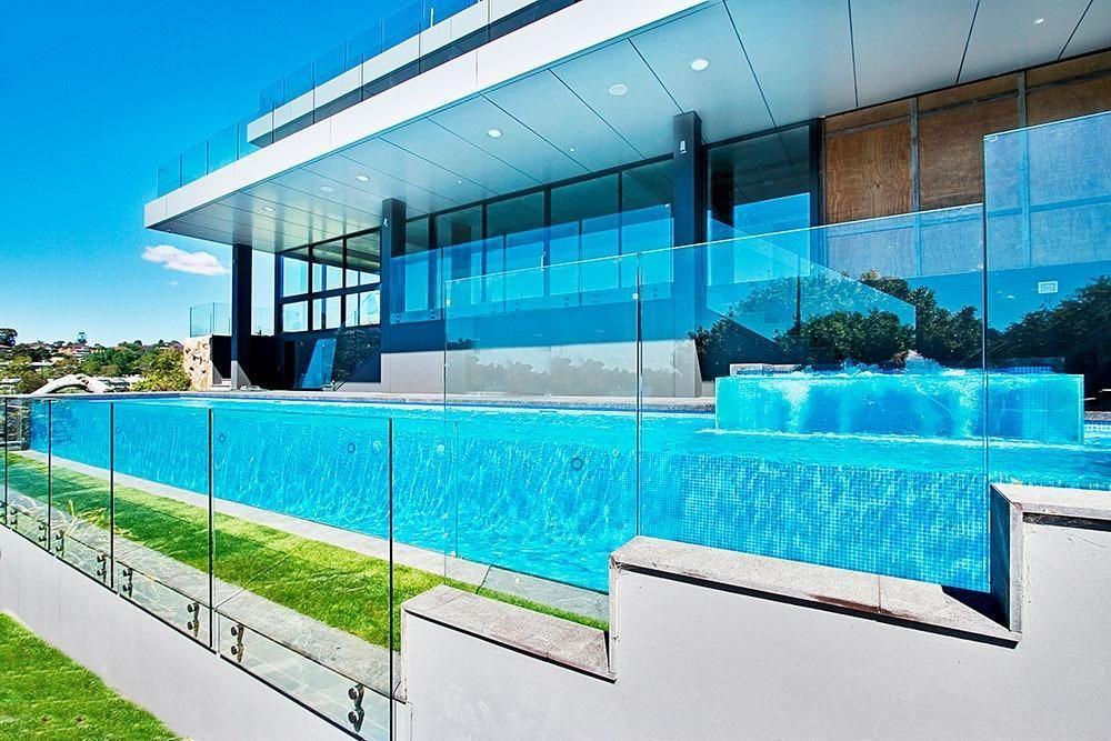 A Large Swimming Pool Is Surrounded By A Glass Fence — Dimension One Glass Fencing In Tuggerah, NSW