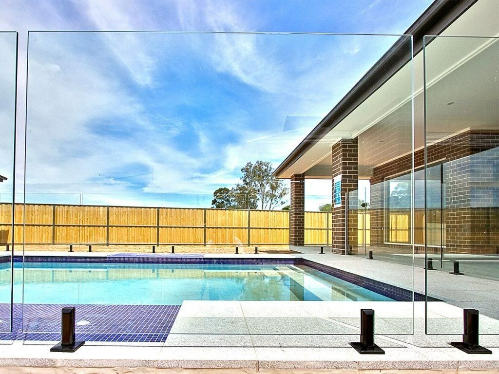 A Large Swimming Pool Is Surrounded By A Glass Fence — Dimension One Glass Fencing In Tuggerah, NSW
