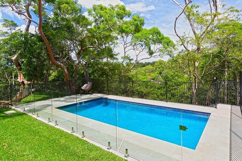 A Large Swimming Pool Surrounded By Trees And Grass In A Backyard — Dimension One Glass Fencing In Tuggerah, NSW