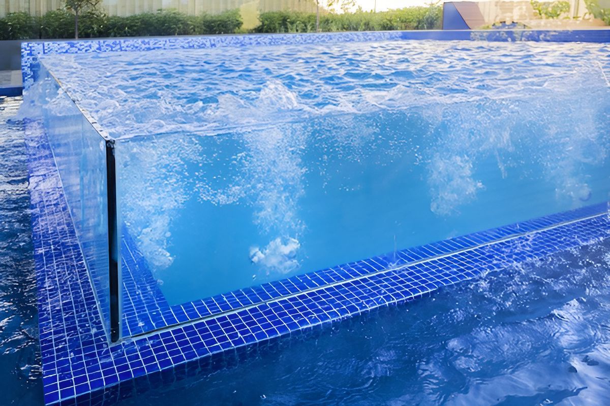 A swimming pool with a clear glass wall and blue tiles — Dimension One Glass Fencing In Tuggerah, NSW