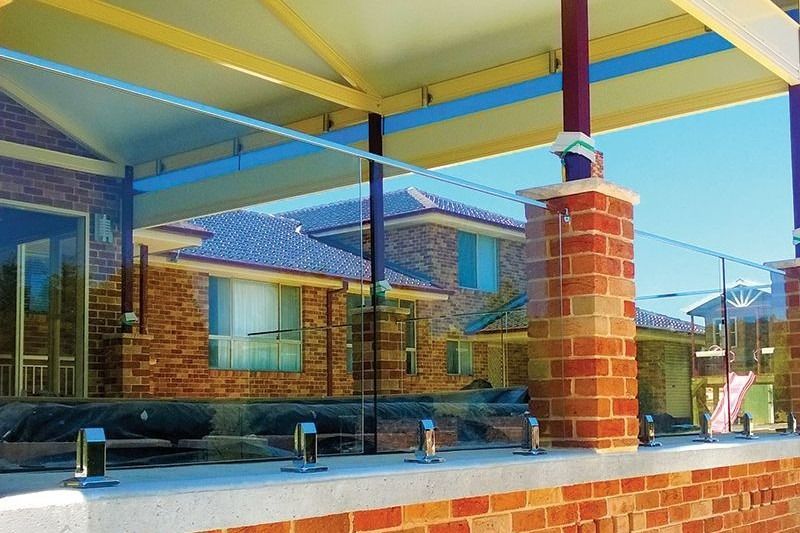 A Brick Building With A Glass Railing Surrounding It — Dimension One Glass Fencing In Central Coast, NSW
