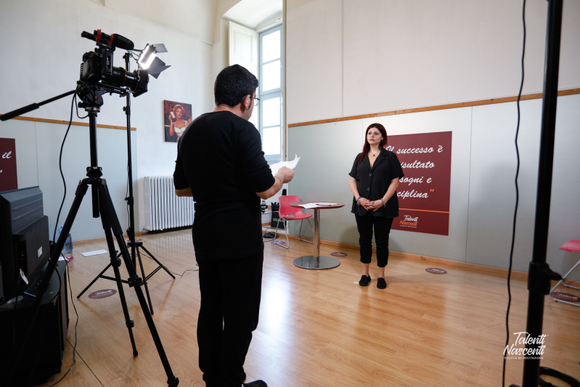 Una persona ne intervista un'altra in uno studio. Sono state predisposte telecamere e luci.