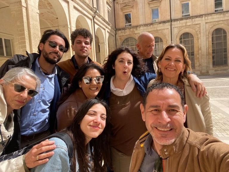 Gruppo di persone sorridenti che si scattano un selfie in un cortile esterno con finestre ad arco.
