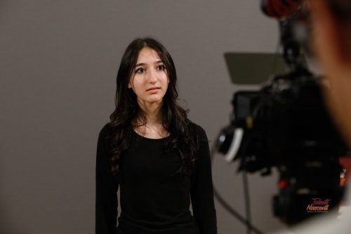 Donna con camicia nera, rivolta verso la telecamera con un'espressione preoccupata, in uno studio fotografico.