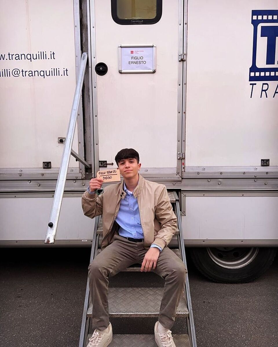 Un uomo con una giacca marrone è seduto sui gradini di una roulotte e alza il pugno.