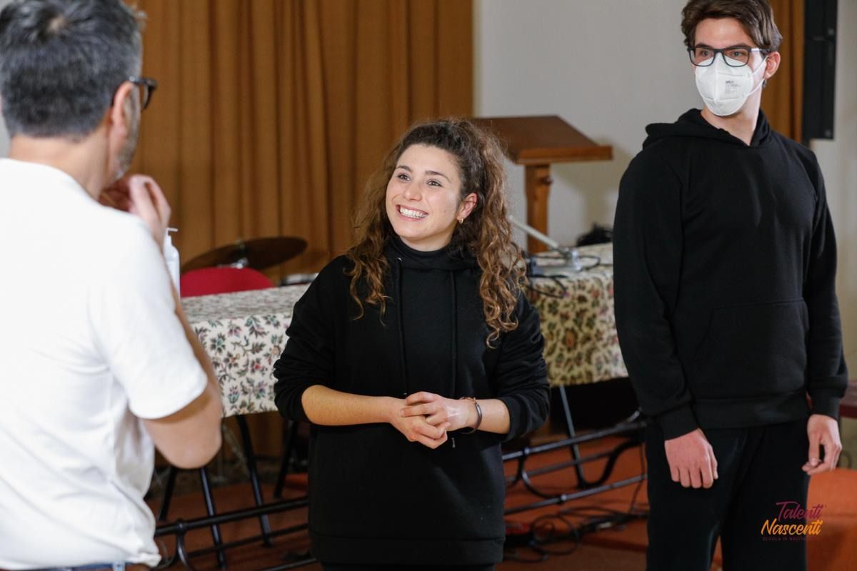 Tre persone in una stanza, due delle quali indossano felpe nere. Una donna sorride, un uomo porta gli occhiali, l'altro indossa una mascherina.