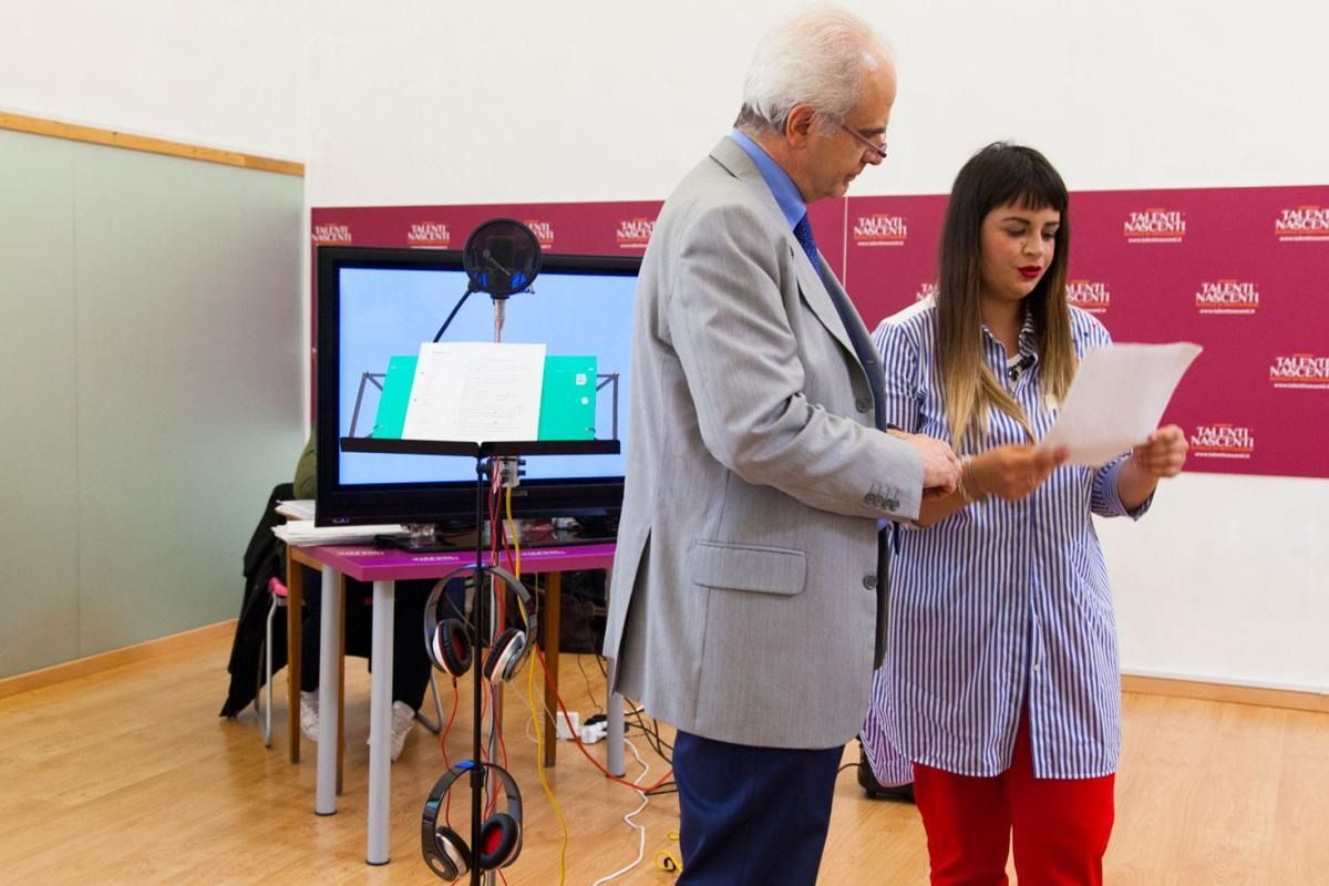Un uomo e una donna rivedono la sceneggiatura in uno studio di registrazione; microfono presente.