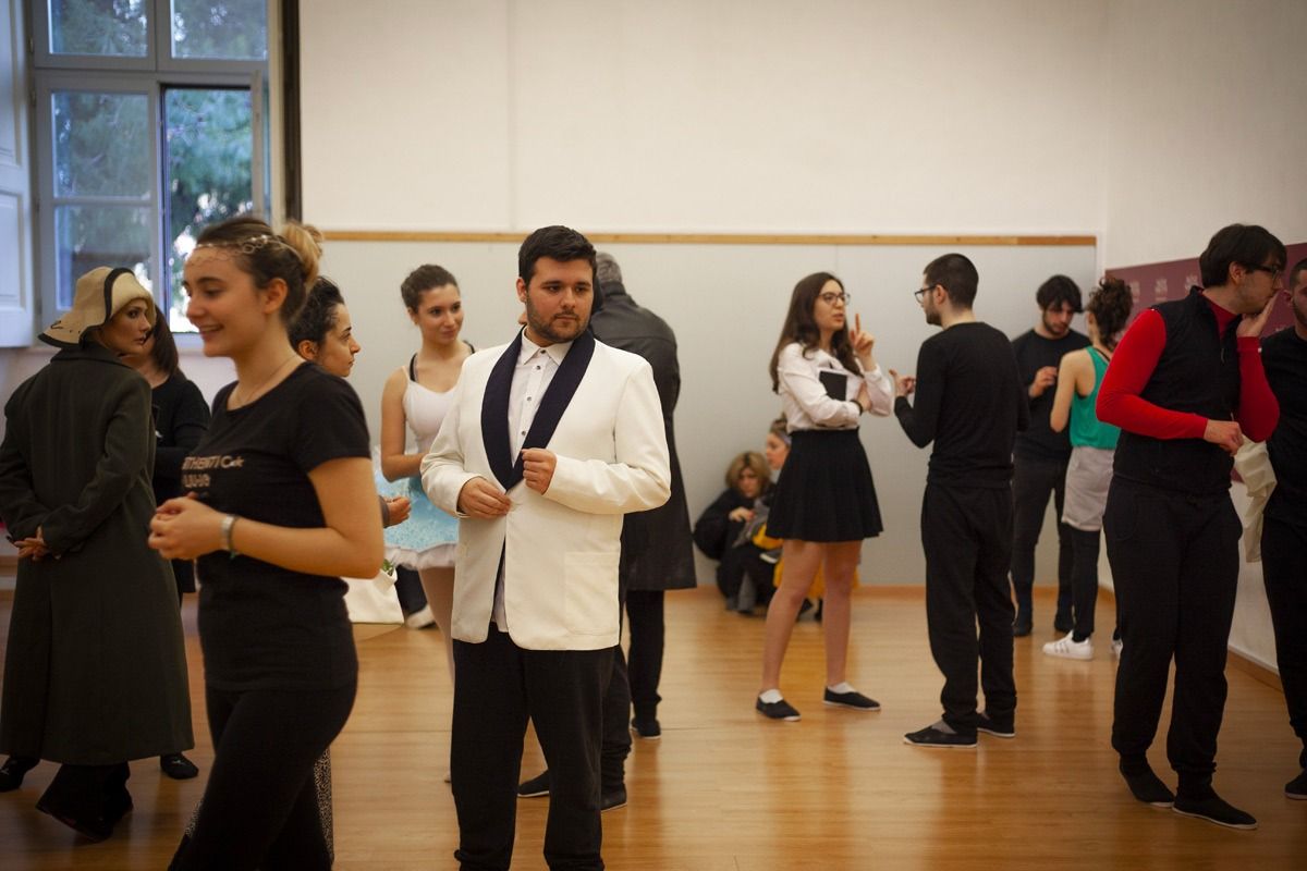 Persone in una sala da ballo, alcune in abiti formali, altre in abiti casual, che si preparano o socializzano.