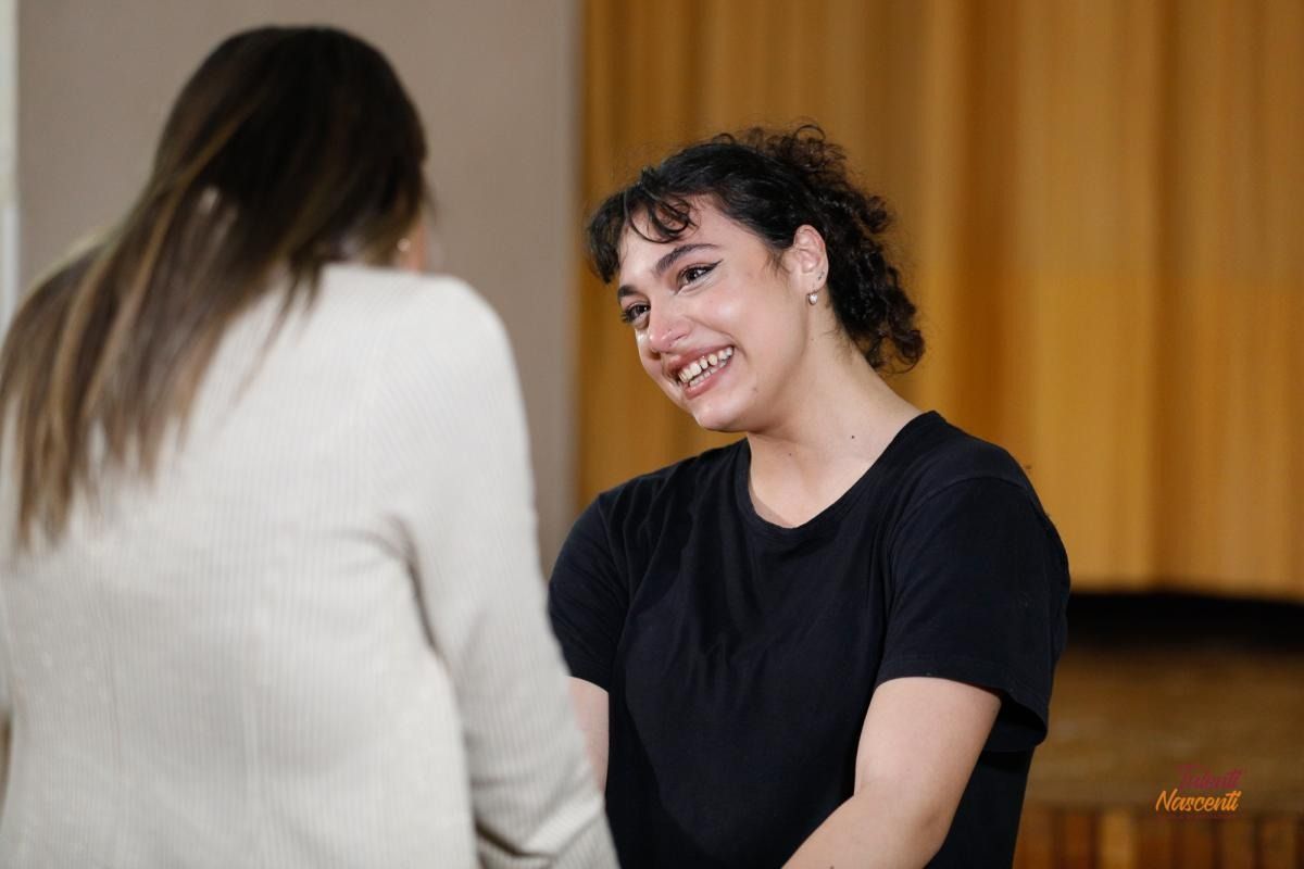 Una donna vestita di nero sorride a un'altra donna in giacca beige in un interno.