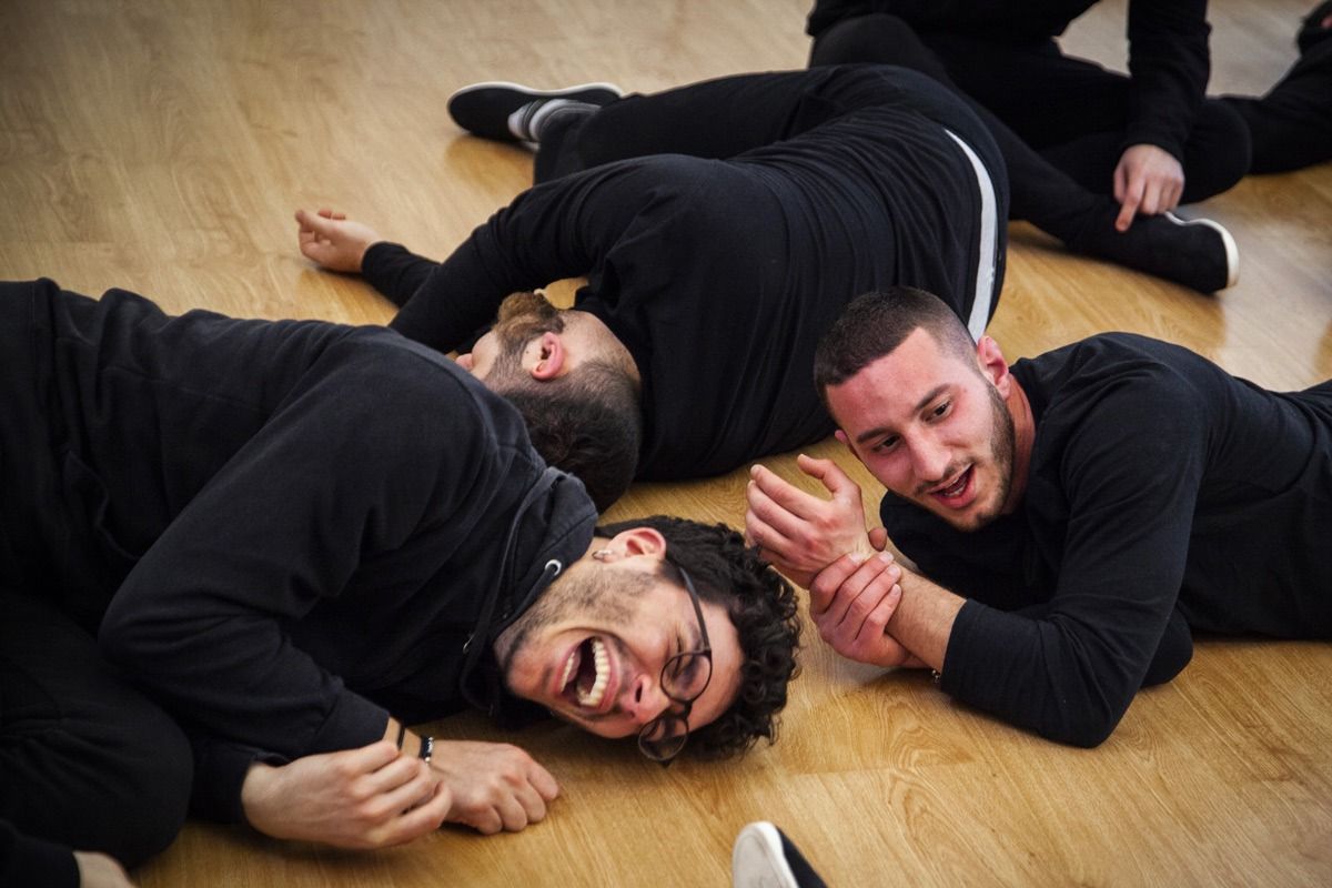 Quattro persone vestite di nero sono sdraiate sul pavimento e ridono.