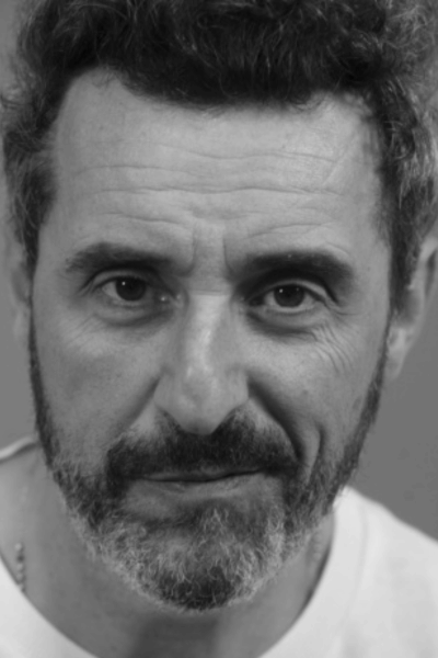 Uomo con barba e capelli corti e brizzolati che guarda direttamente l'osservatore.