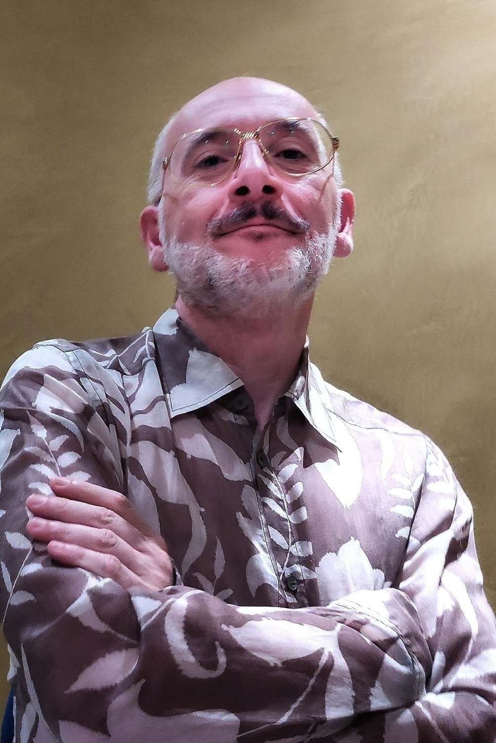 Uomo con gli occhiali, braccia incrociate, camicia a fantasia, sorridente.