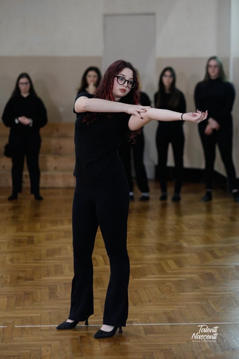 Donna vestita di nero che balla con le braccia tese davanti ad altre persone.