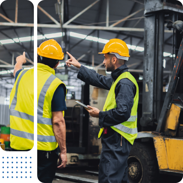 Two men wearing hard hats and safety vests are standing in front of a forklift.