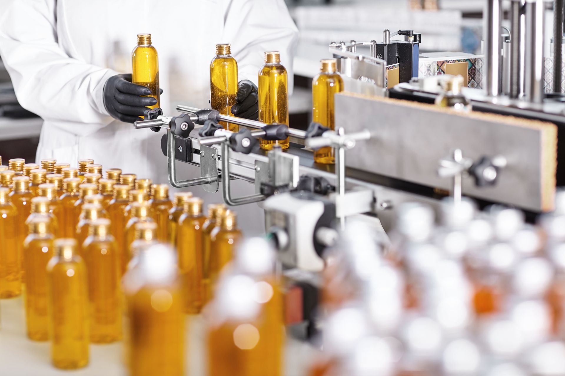 A scientist is holding a bottle in front of a conveyor belt filled with bottles.