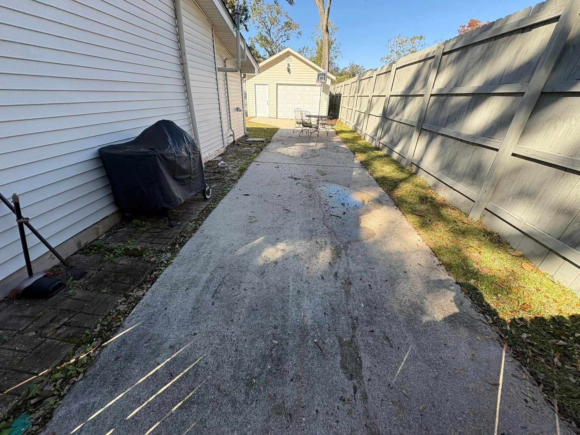 A concrete walkway leading to a house next to a fence.