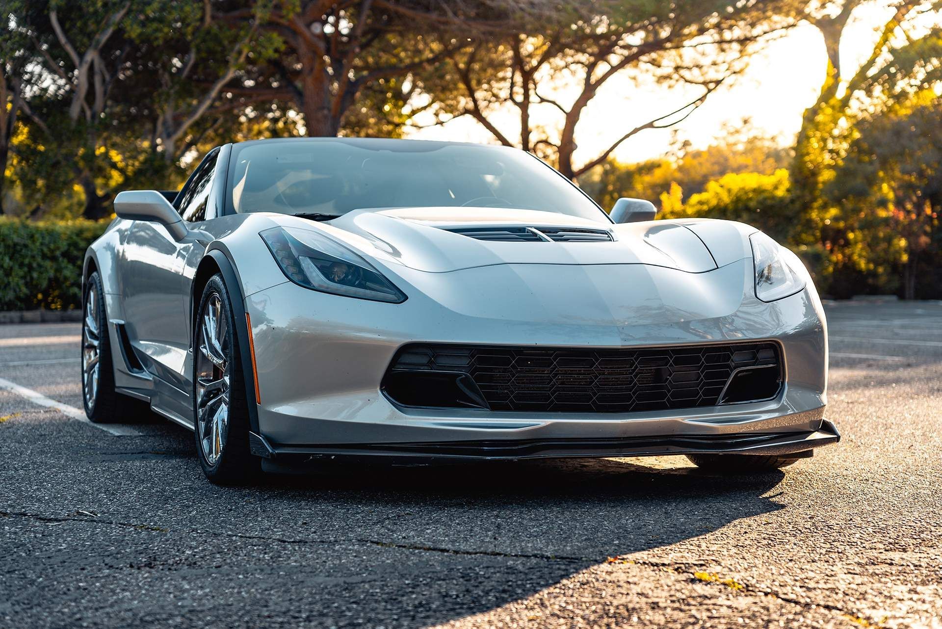 White sports car parked on a road at sunset, with trees and warm light in the background