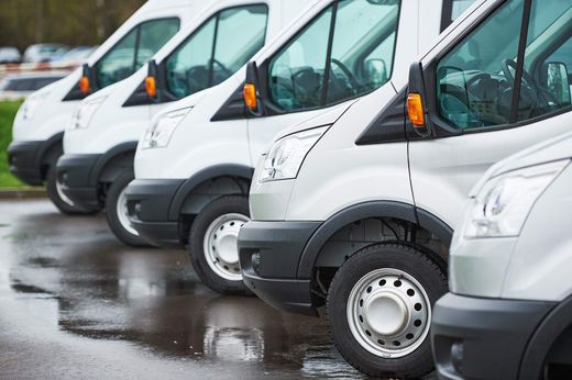 Row of white delivery vans parked on a wet lot