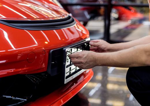 Hands fitting a license plate on the front of a red car in a garage