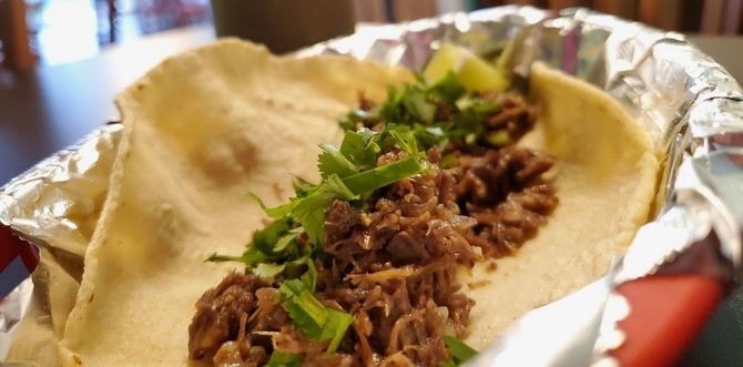 A close up of a row of tacos with meat , cilantro and onions.