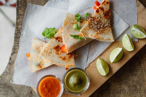 A wooden cutting board topped with quesadillas , limes and sauces.