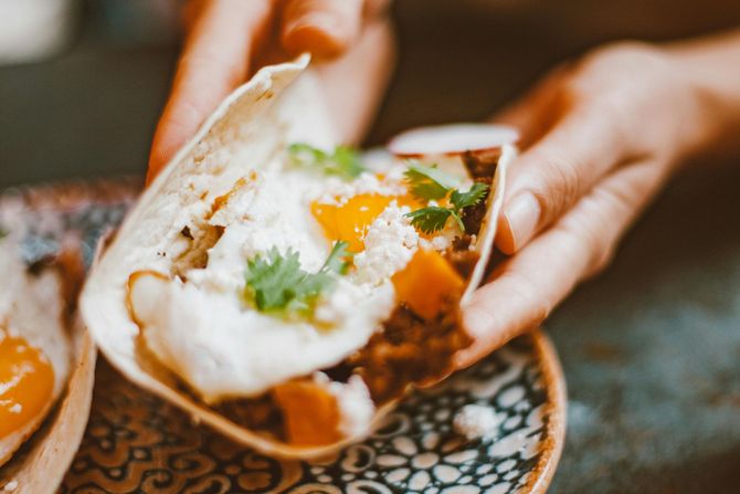 A person is holding a taco in their hands on a plate.