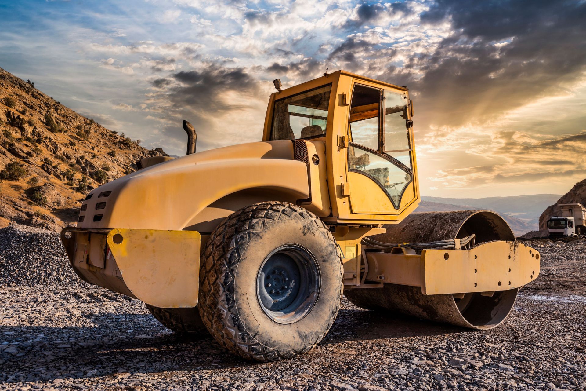 A yellow road roller is sitting on top of a gravel road.