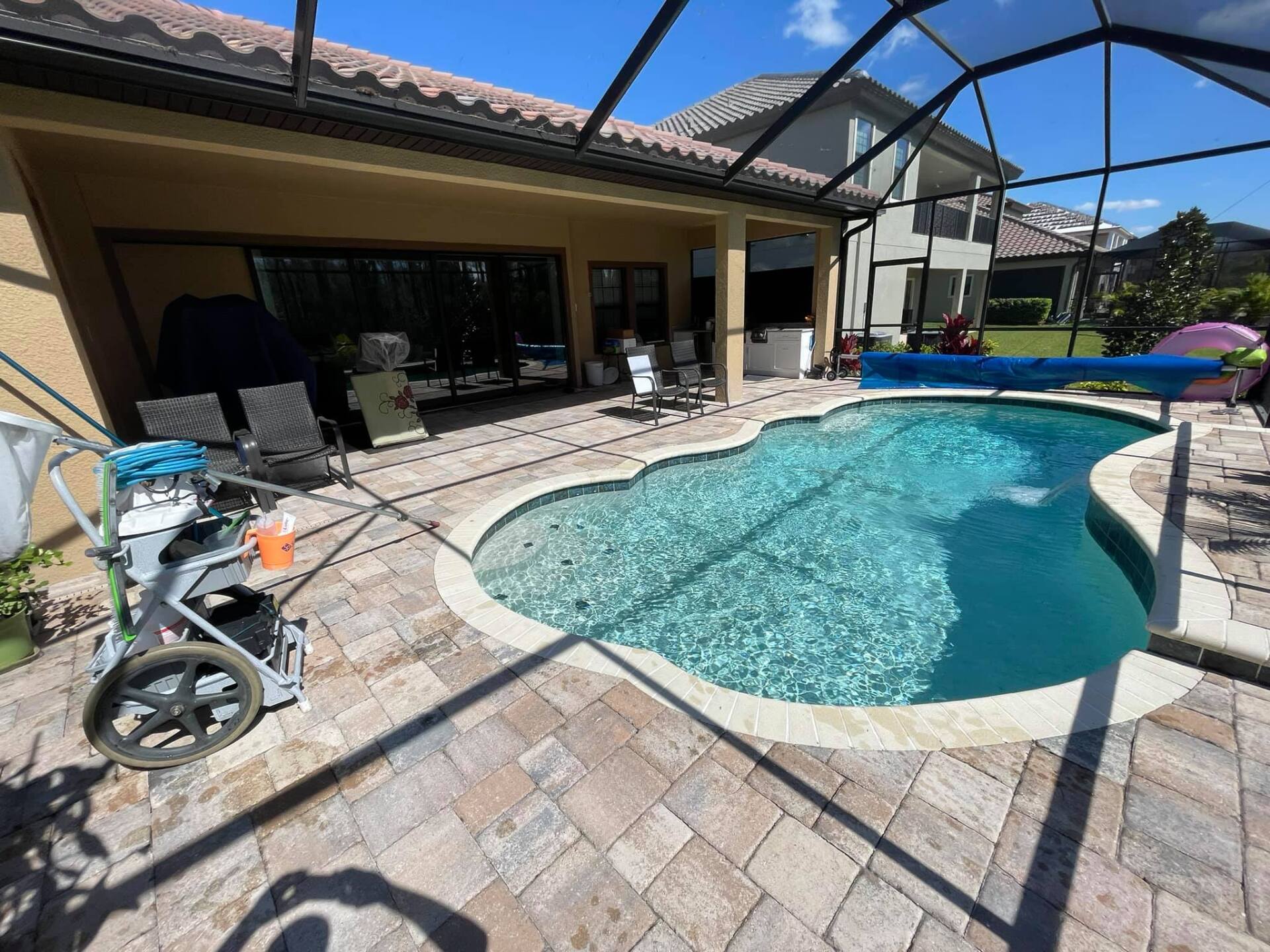 Backyard with pool, patio, and house. Pool equipment nearby. Sunny day.