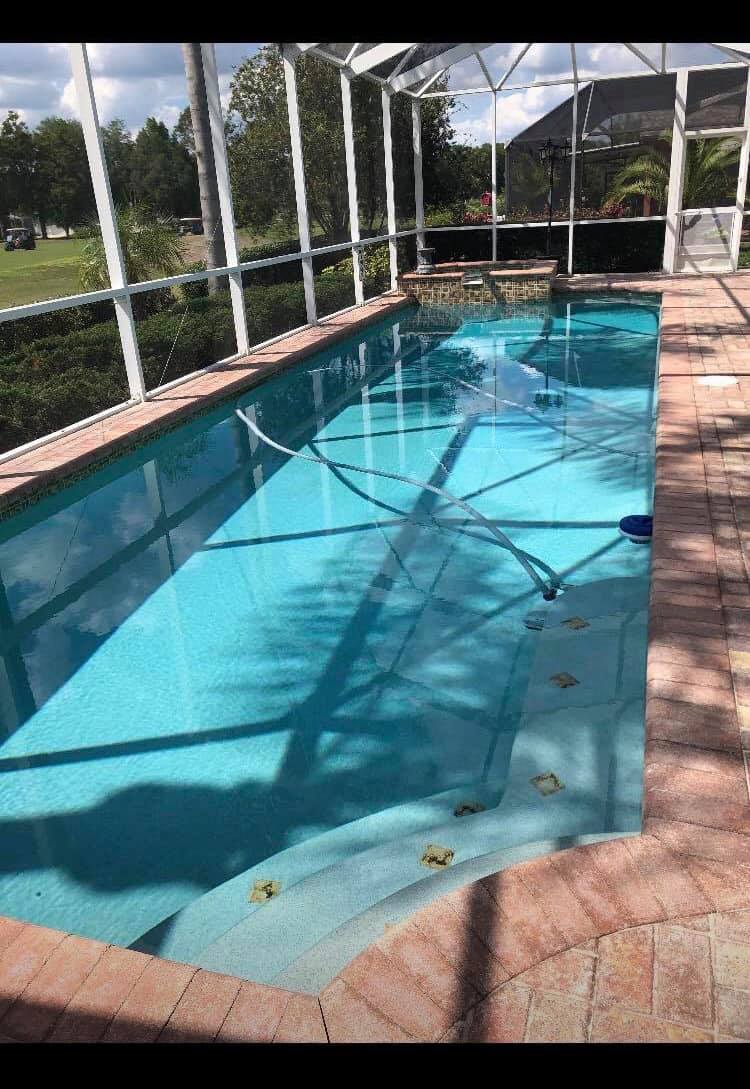 Pool surrounded by a screened enclosure, with turquoise water, brick patio, and steps.