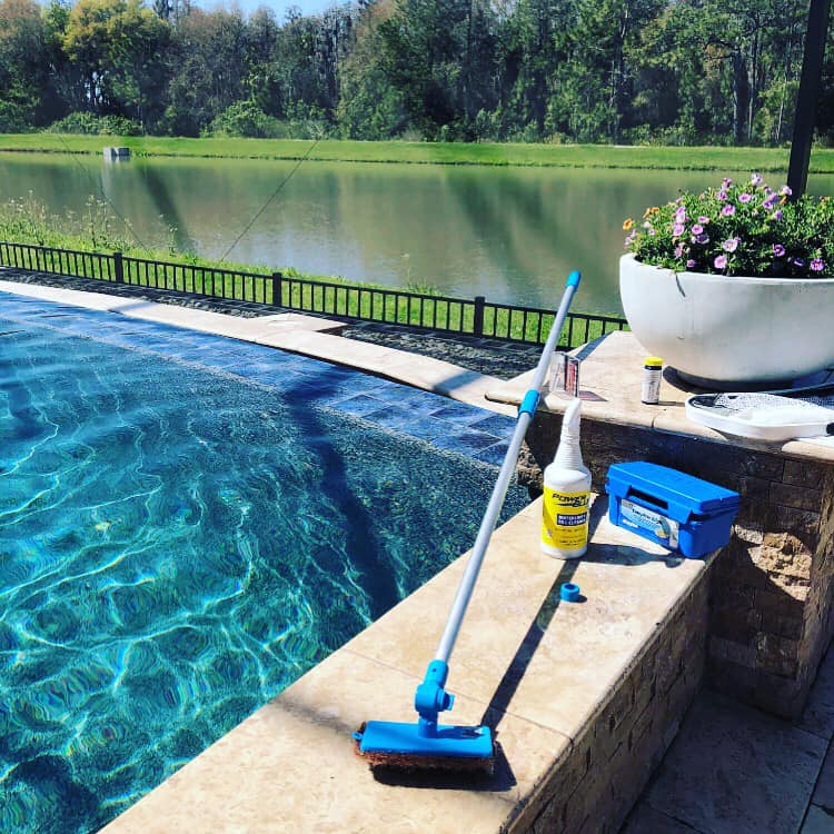 Poolside scene: blue water, cleaning supplies, overlooking a lake.