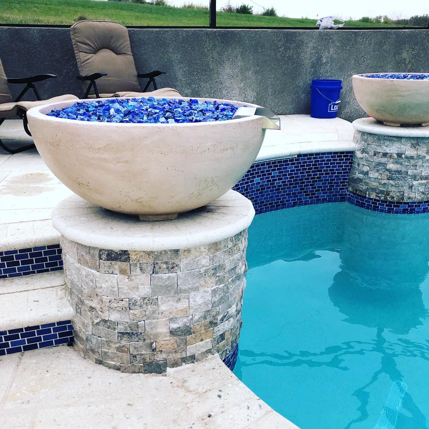 Poolside fire bowl with blue glass, stone pillar, and turquoise water.
