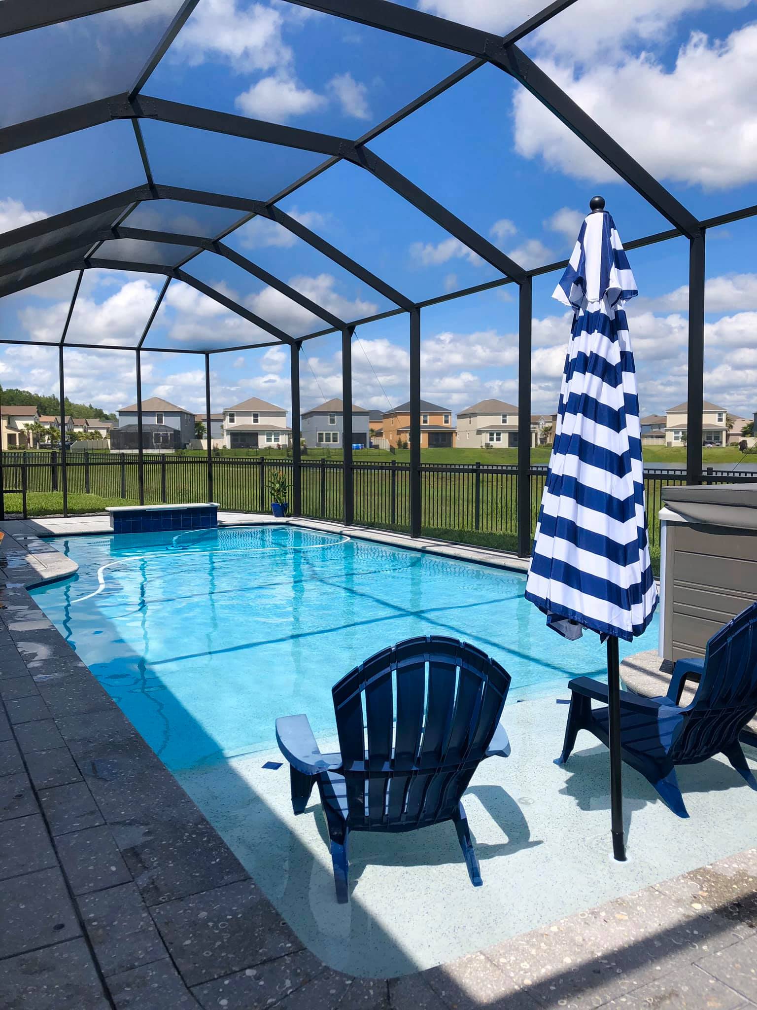 Swimming pool with blue water, surrounded by a screened-in enclosure, lounge chairs, and blue and white striped umbrella.