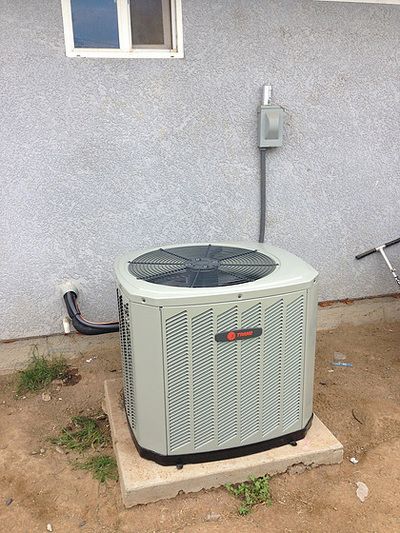 An air conditioner is sitting outside of a house next to a window.