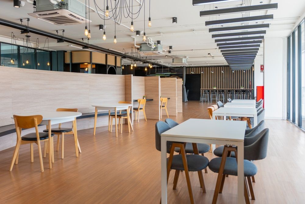 Modern open office with wooden tables, chairs, and pendant lights in a bright workspace