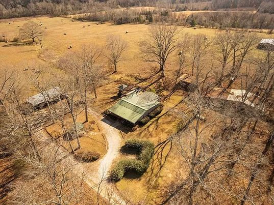 An aerial view of a house in the middle of a field surrounded by trees.