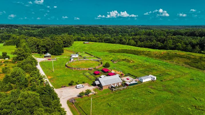 An aerial view of a farm in the middle of a lush green field surrounded by trees.