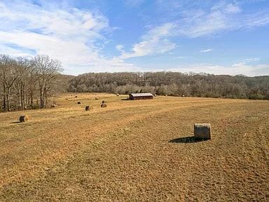 A field filled with hay bales and a barn in the background.