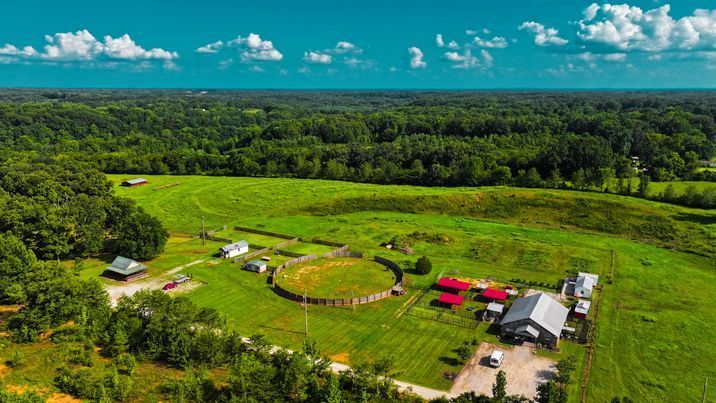 An aerial view of a farm in the middle of a lush green field surrounded by trees.