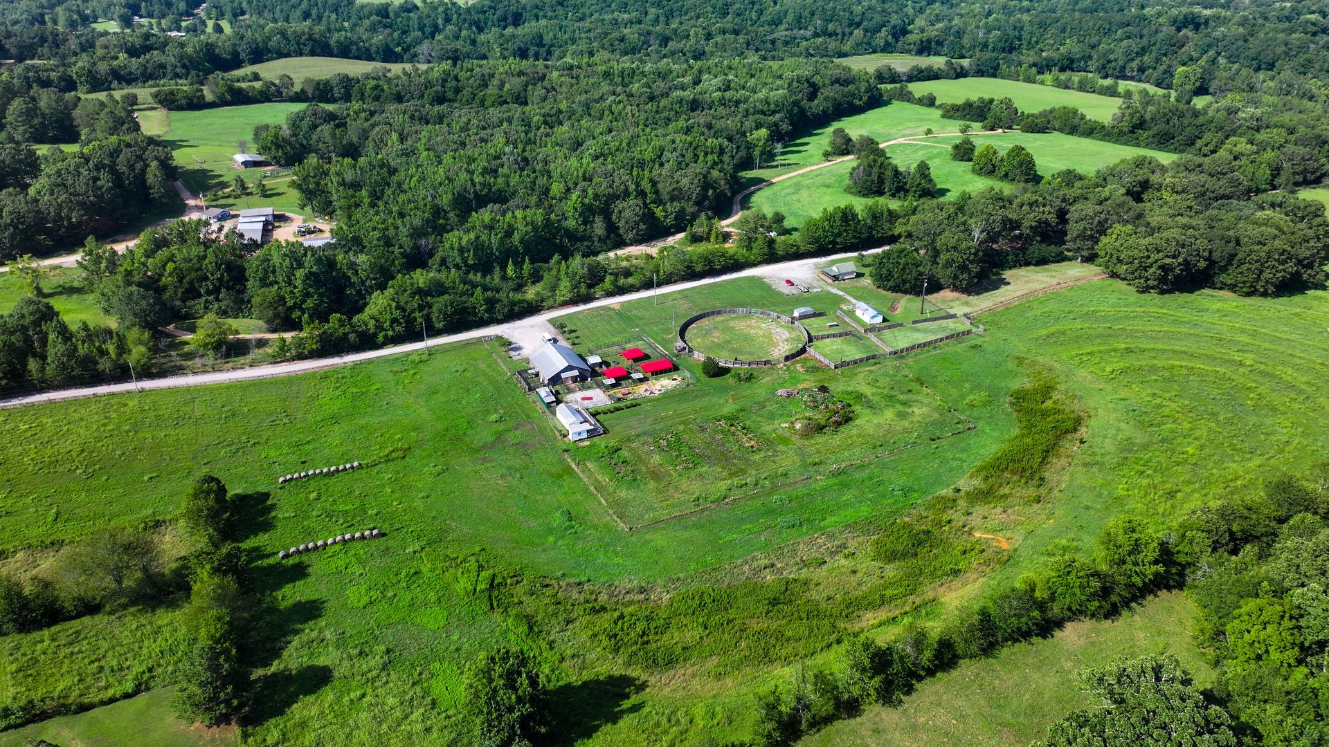 An aerial view of a large green field surrounded by trees and a road.