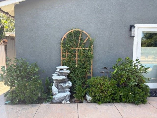 Backyard garden with climbing trellis, stone fountain, and lush greenery against a gray wall.