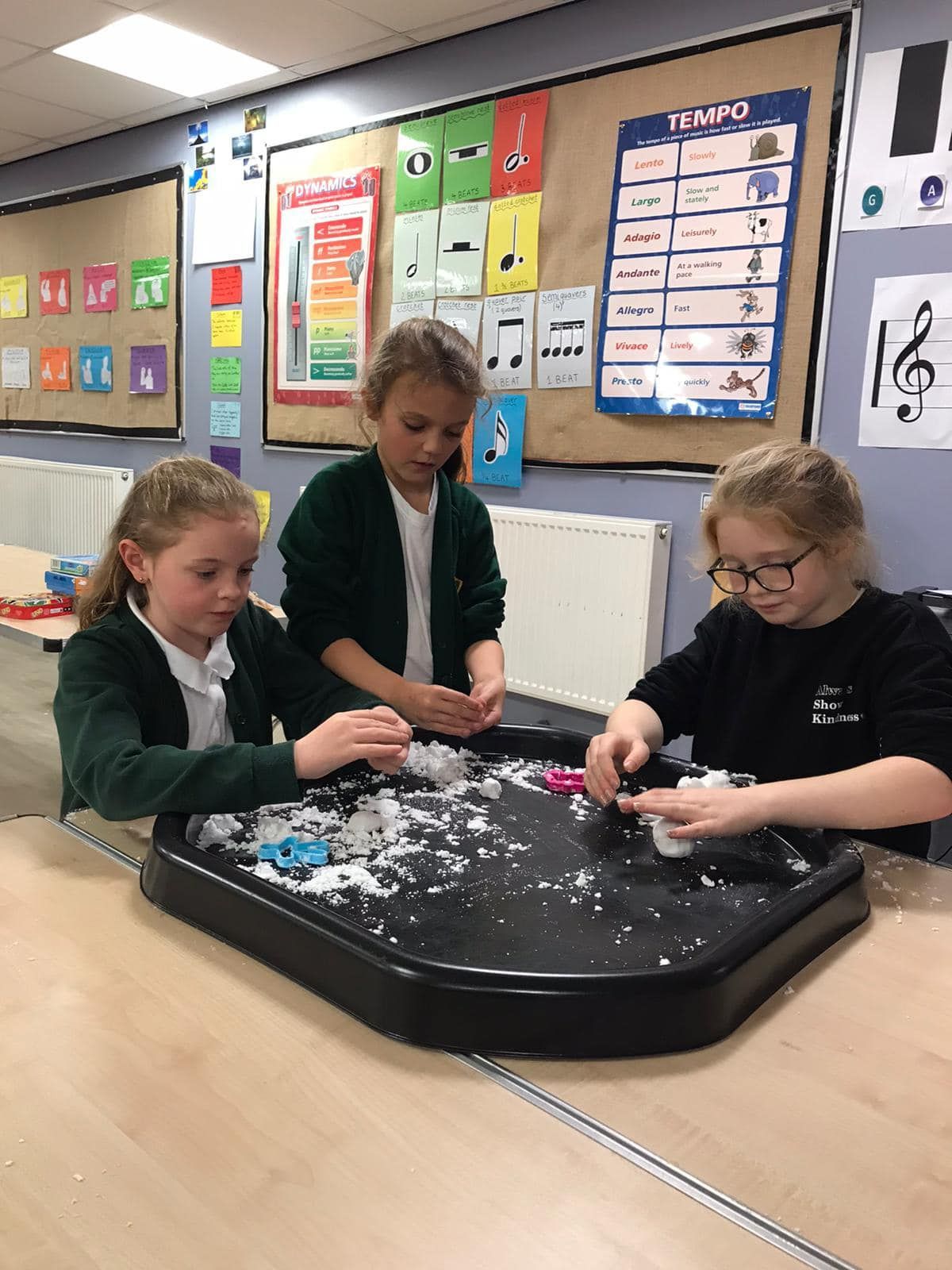 Three young girls are playing with snow in a classroom.