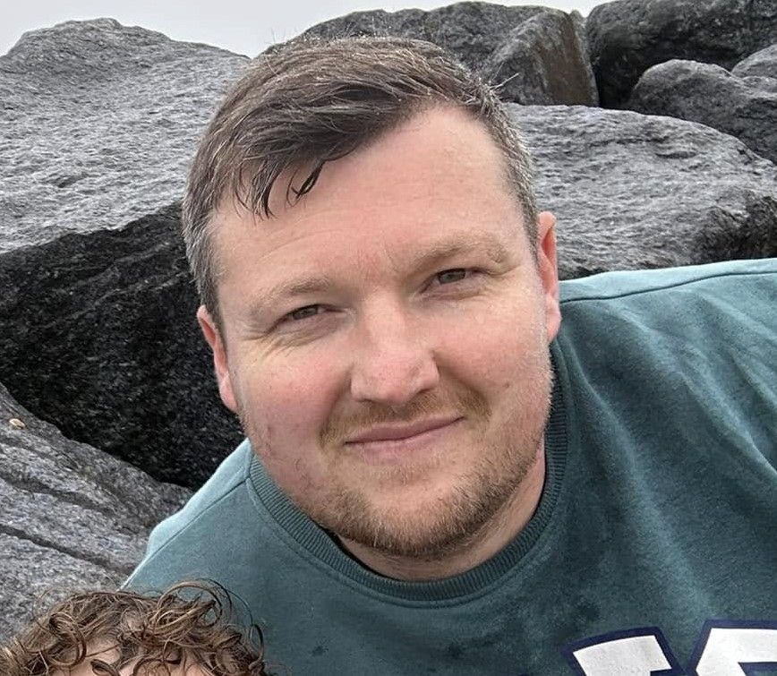 A man in a green shirt is standing next to a child on a rocky beach.