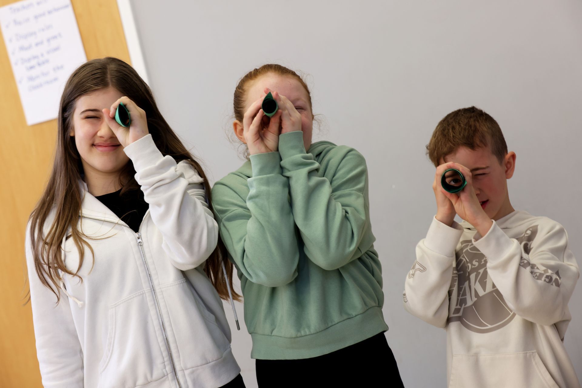 A boy and two girls are looking through binoculars.