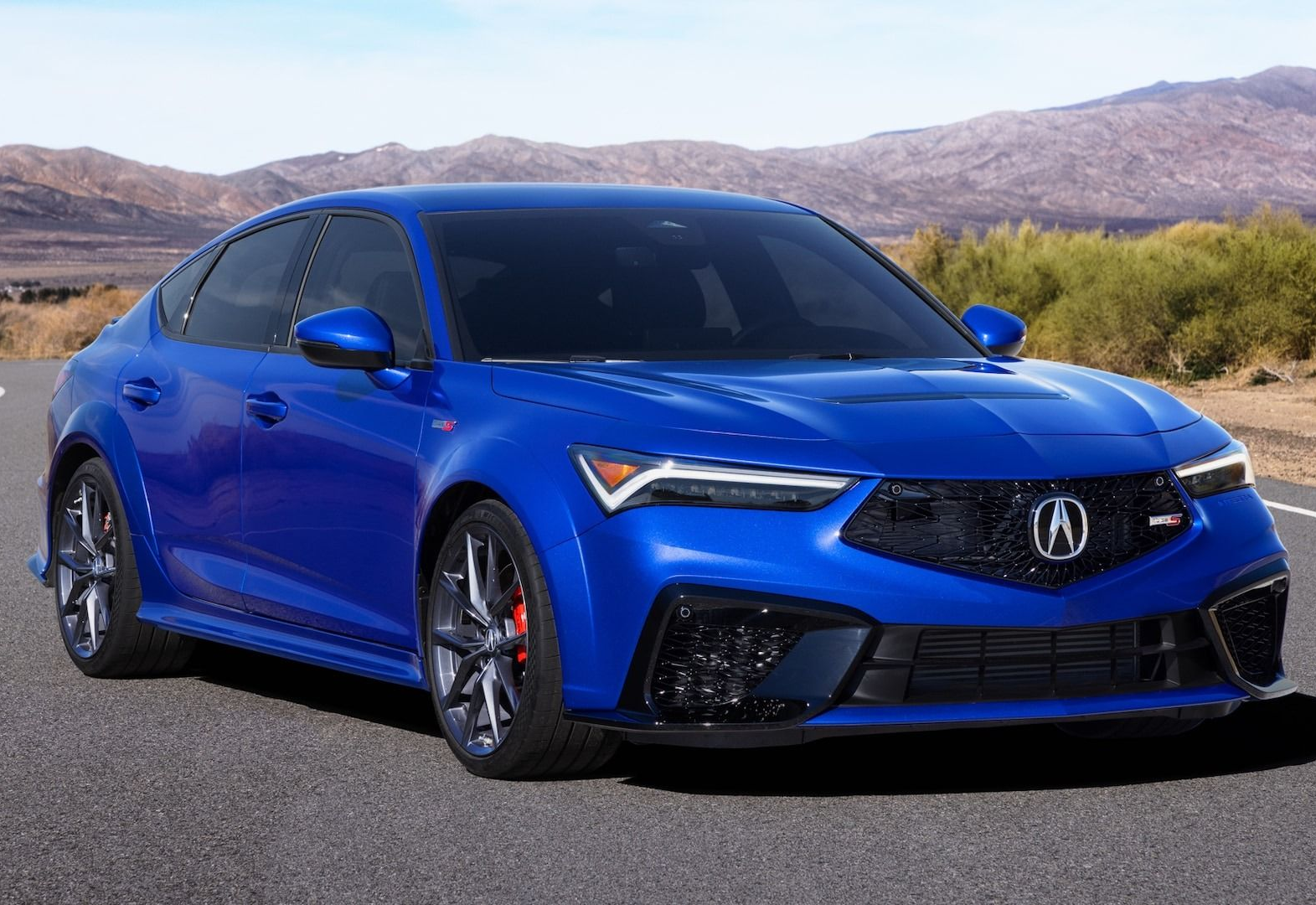 Blue Acura Integra Type S on a paved road with a mountain background.