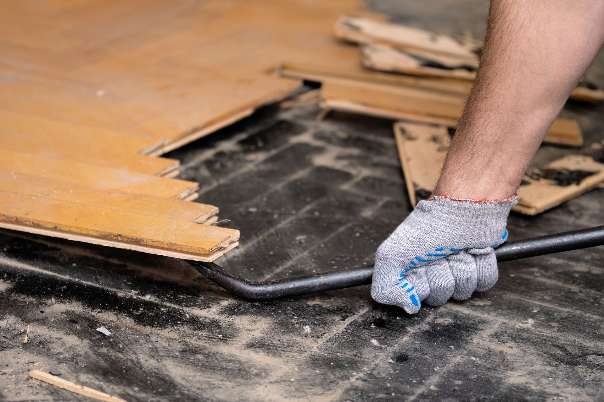 Worker prying up damaged hardwood flooring with a pry bar during demolition.