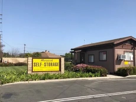 A self-storage facility entrance. Sign with yellow text on brown and tan walls, brown building, blue sky.