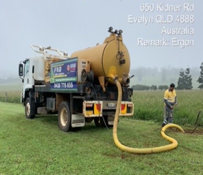 Vacuum truck parked in a field, a worker attending a hose. Evelyn, Australia.